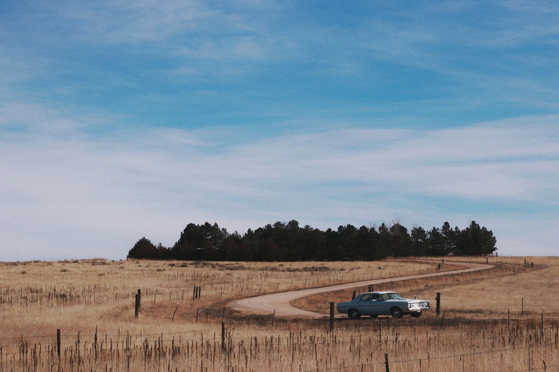 Vintage car on a winding dirt road through fenced pasture